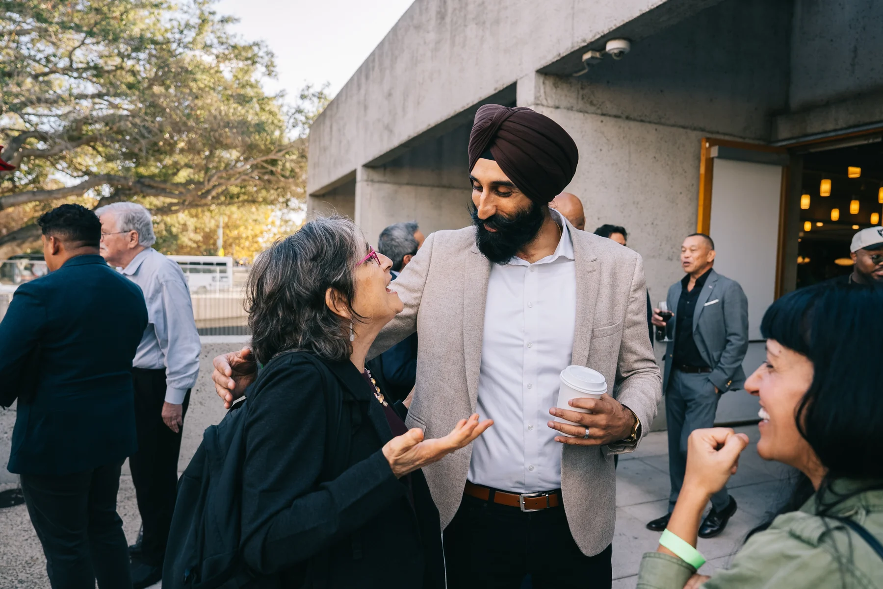Guests talk together outside, including a man in a turban with his arm around another guest.