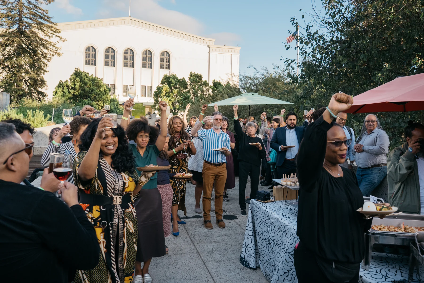 Guests raise their fists and glasses together in the museum courtyard.