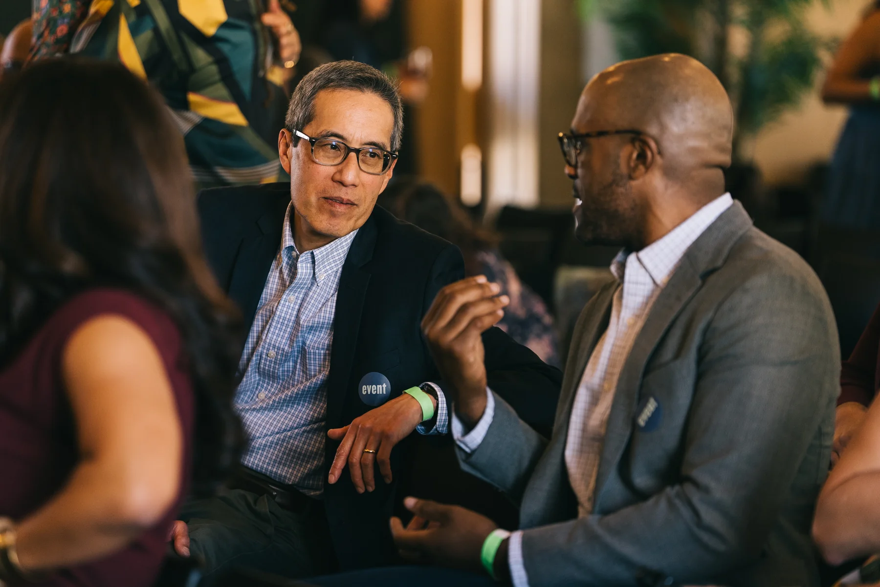 Two seated guests in jackets lean toward one another in conversation.