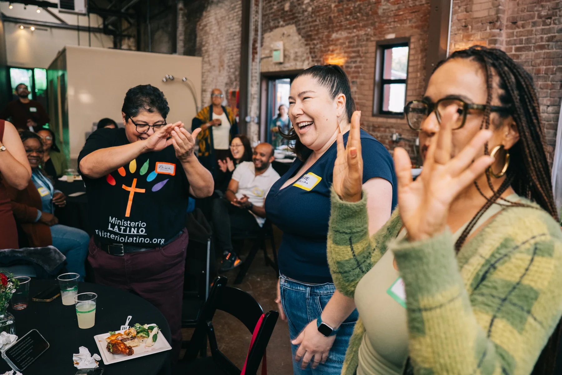 Attendees stand beside a table, laughing with their hands raised.