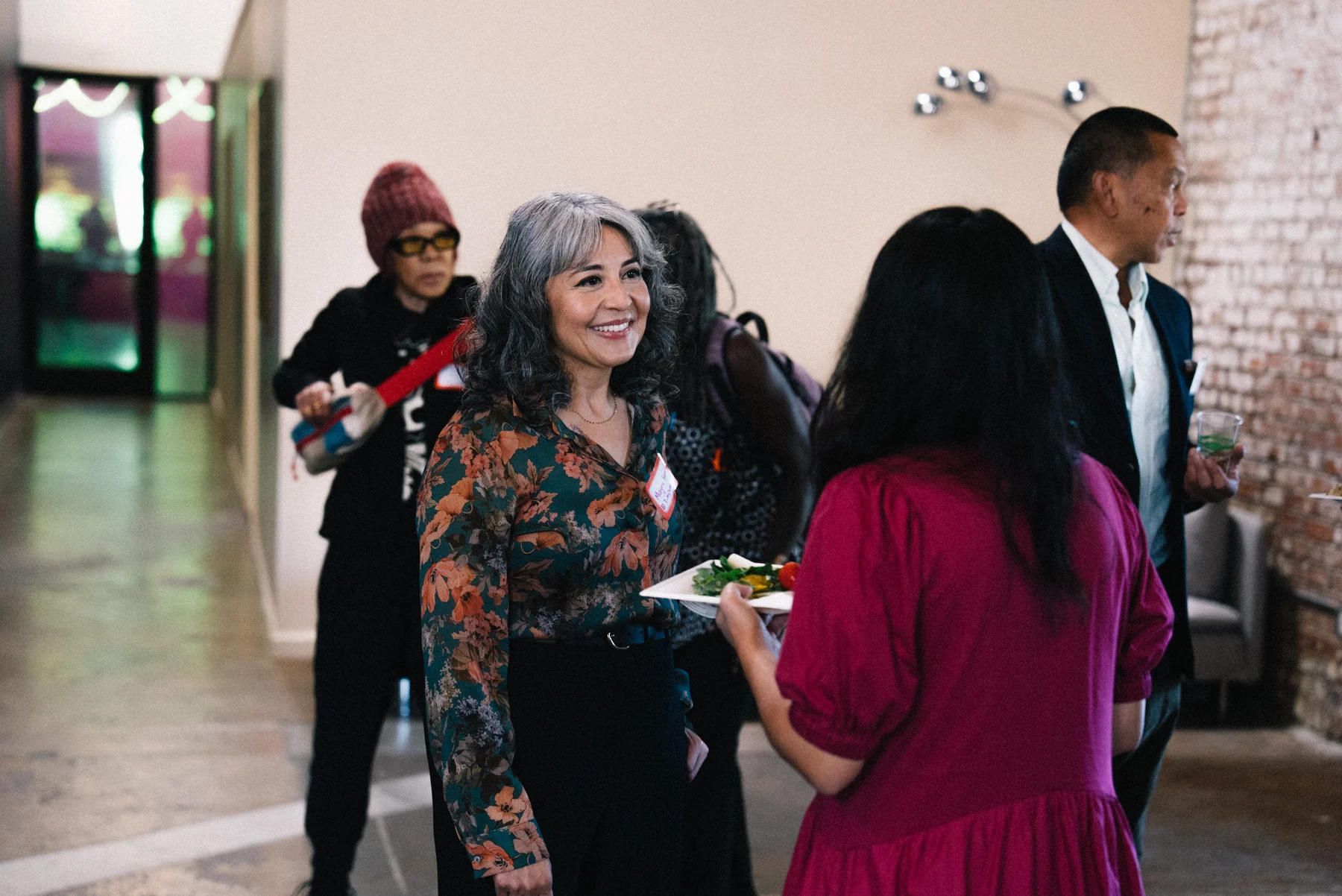 Attendees greet one another inside the venue, including a smiling guest in a floral shirt.