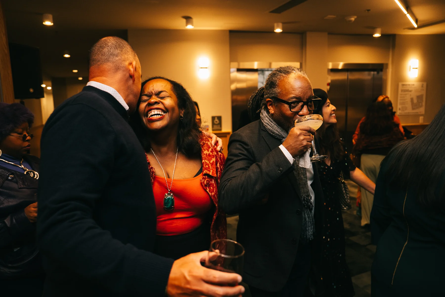 A guest in red laughs during a conversation as another guest raises a glass.