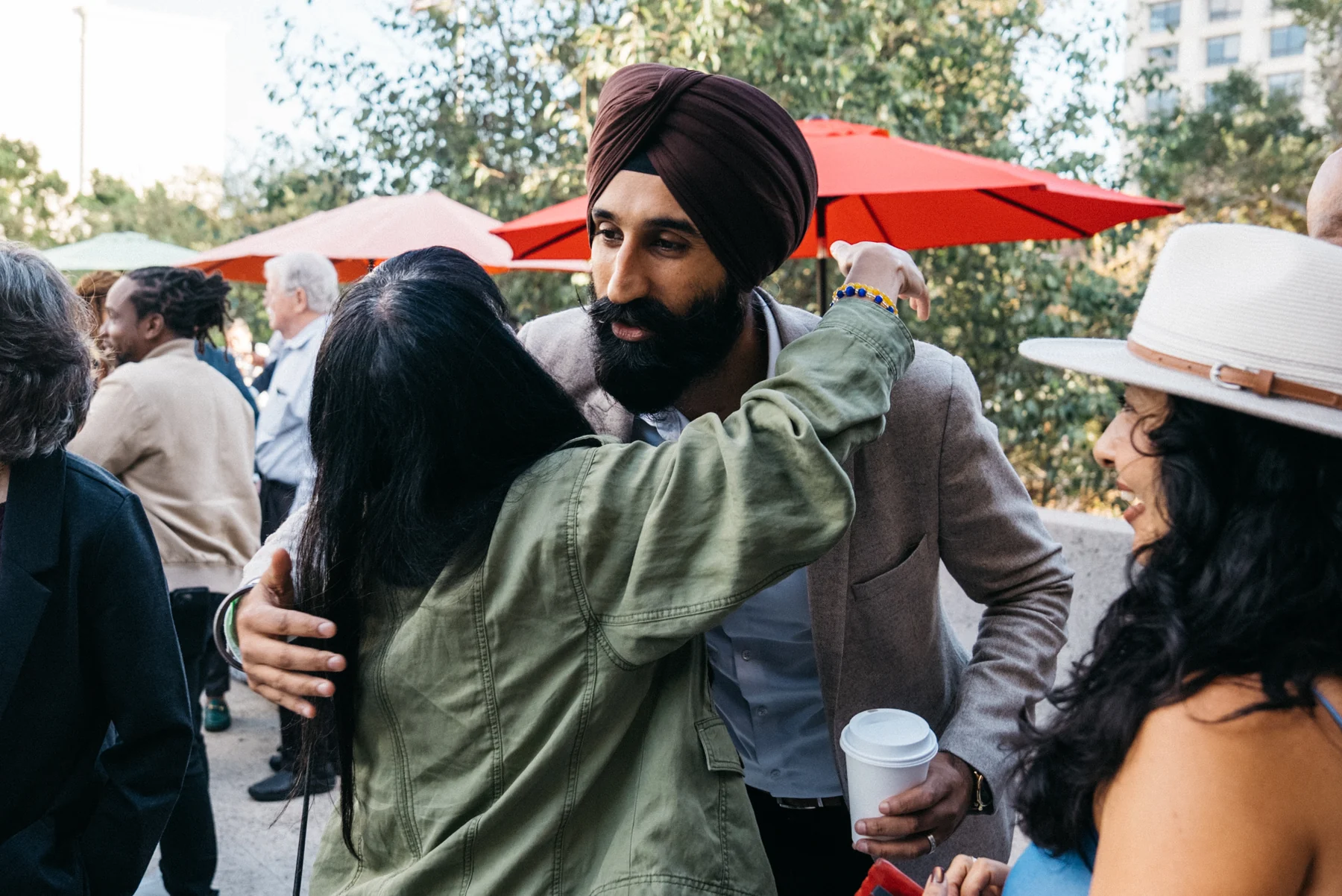 Two guests embrace during the outdoor reception as another guest smiles nearby.