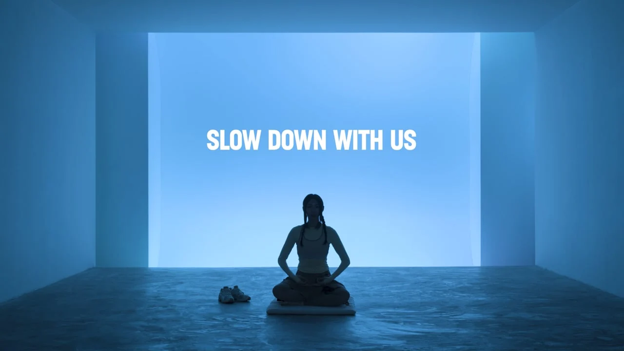 A seated figure in a blue-lit room beneath the words Slow Down With Us.