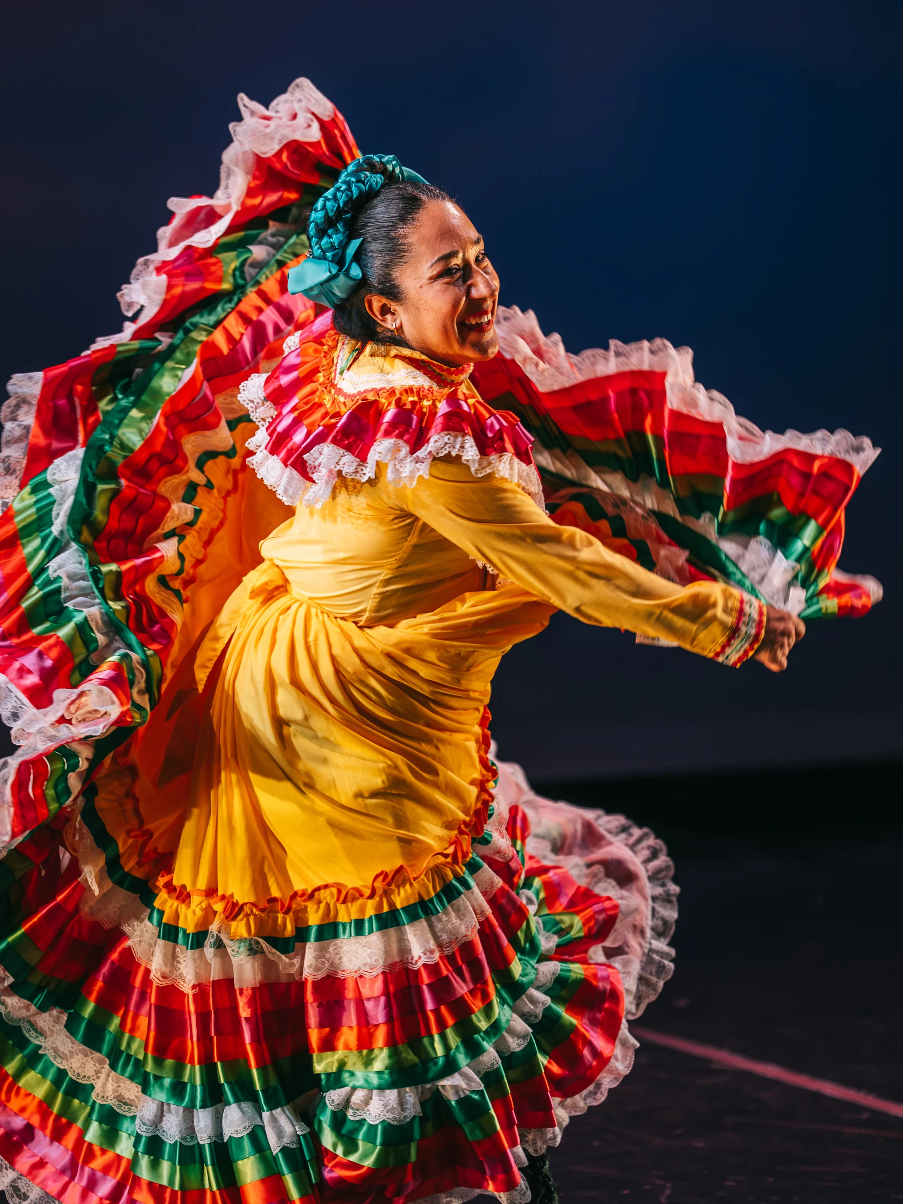 A dancer in a yellow dress sweeps red, green and white ruffles around them on stage.
