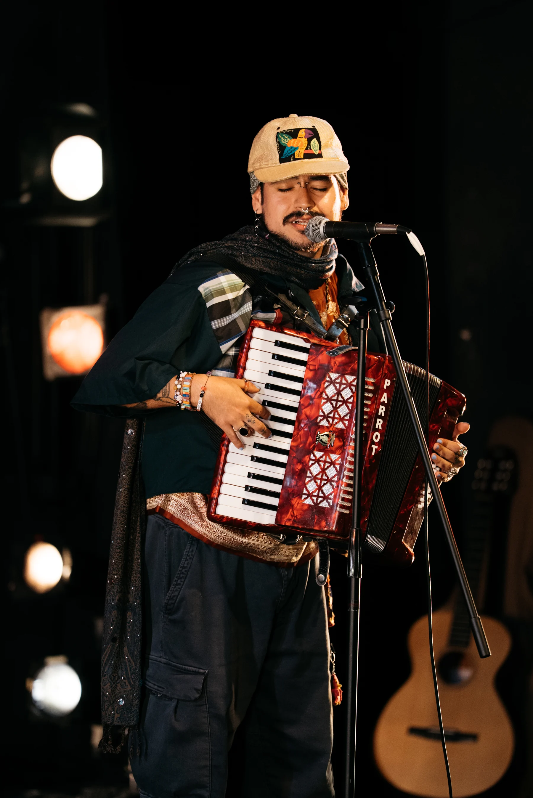 A musician plays a red accordion at a microphone, with an acoustic guitar behind them.