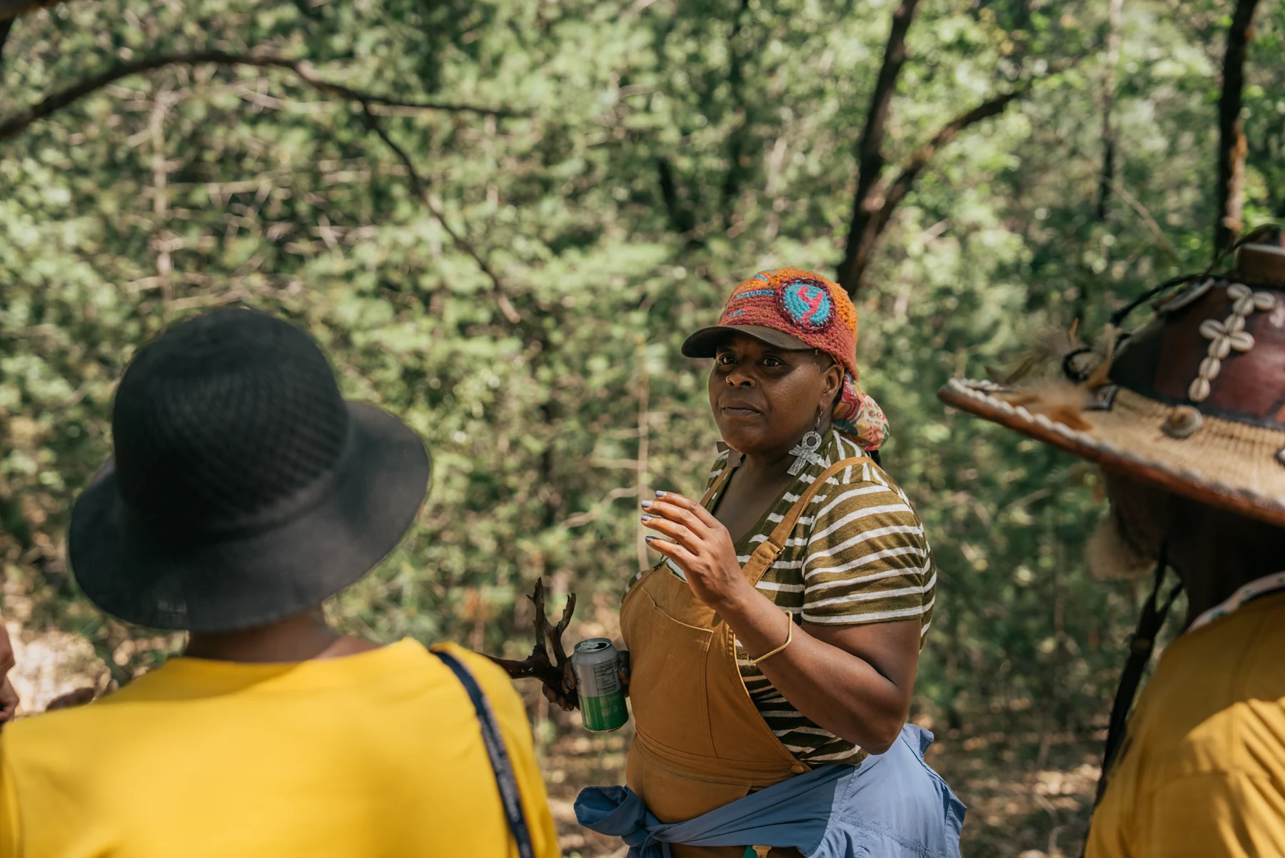 A participant gestures while talking with others beneath the trees.