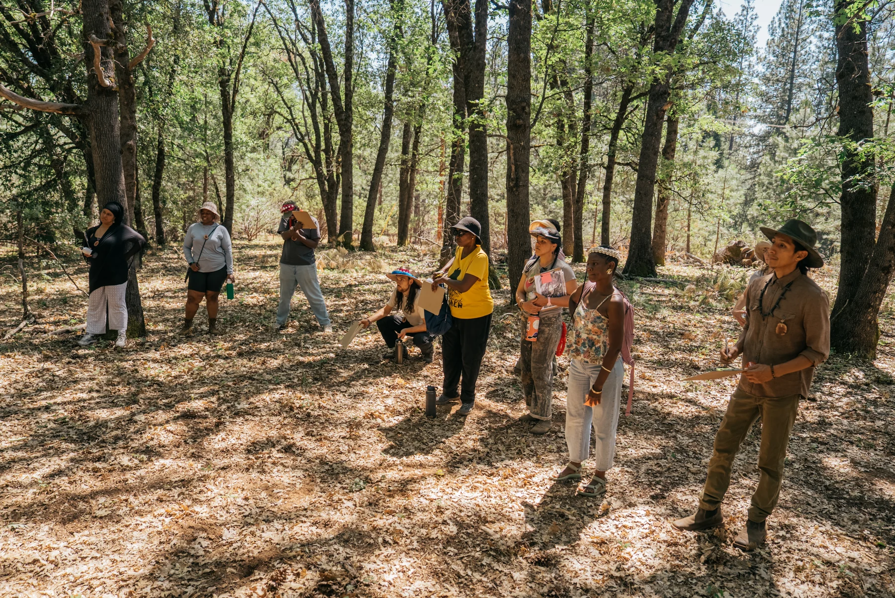 Participants carrying planning materials listen together among the trees during a tour of the land.