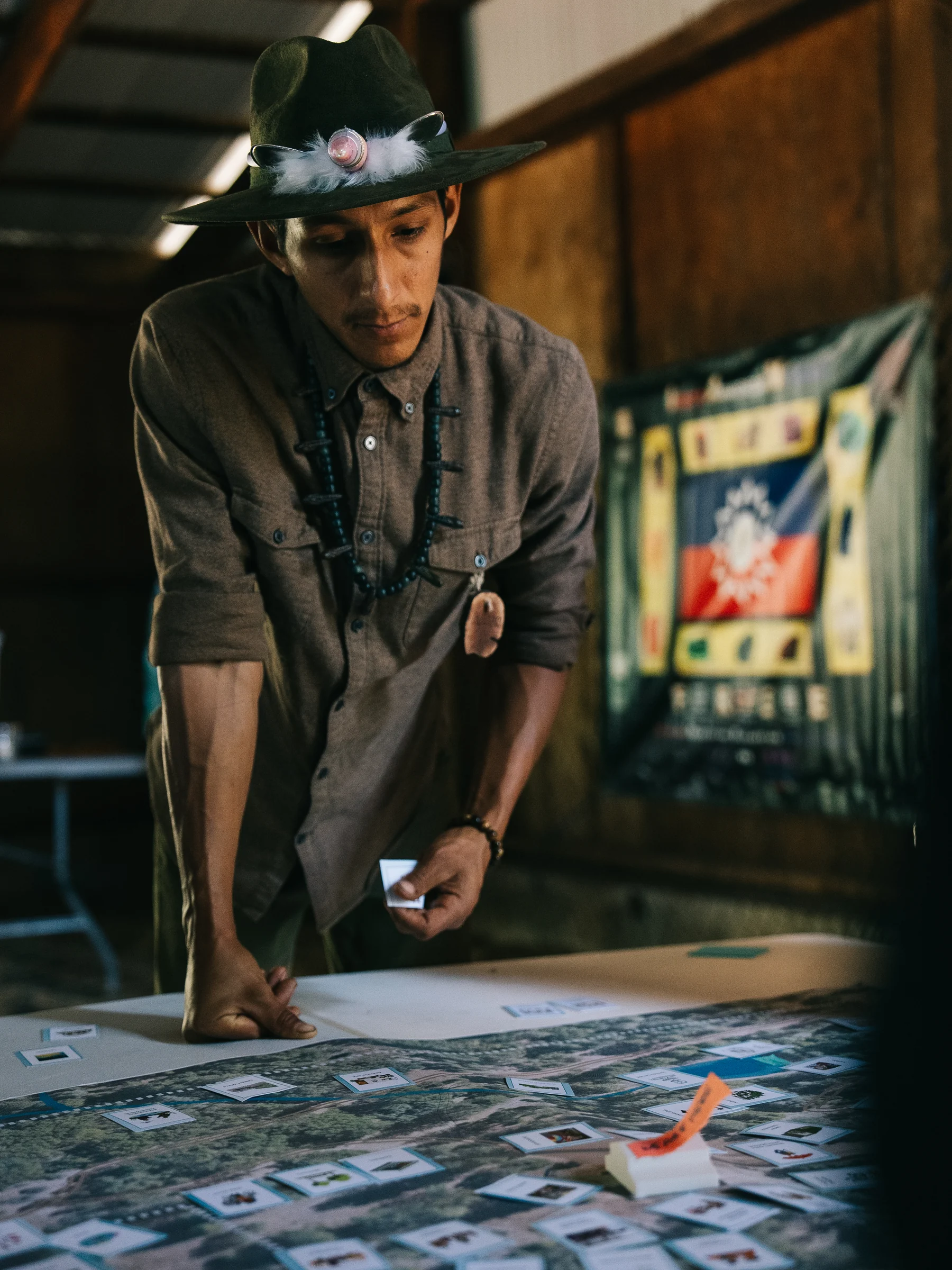 A participant in a feathered hat leans over a table covered with photographs and design materials.