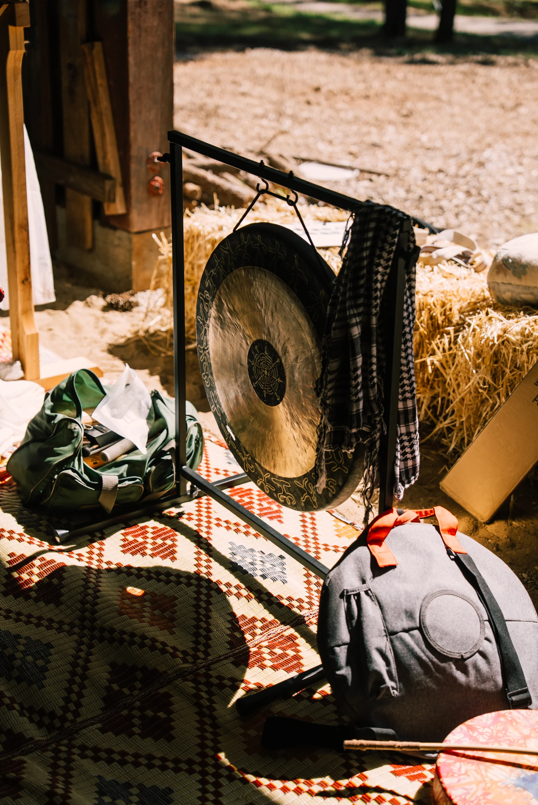 A gong, bags and patterned rugs sit near an open doorway in warm afternoon light.