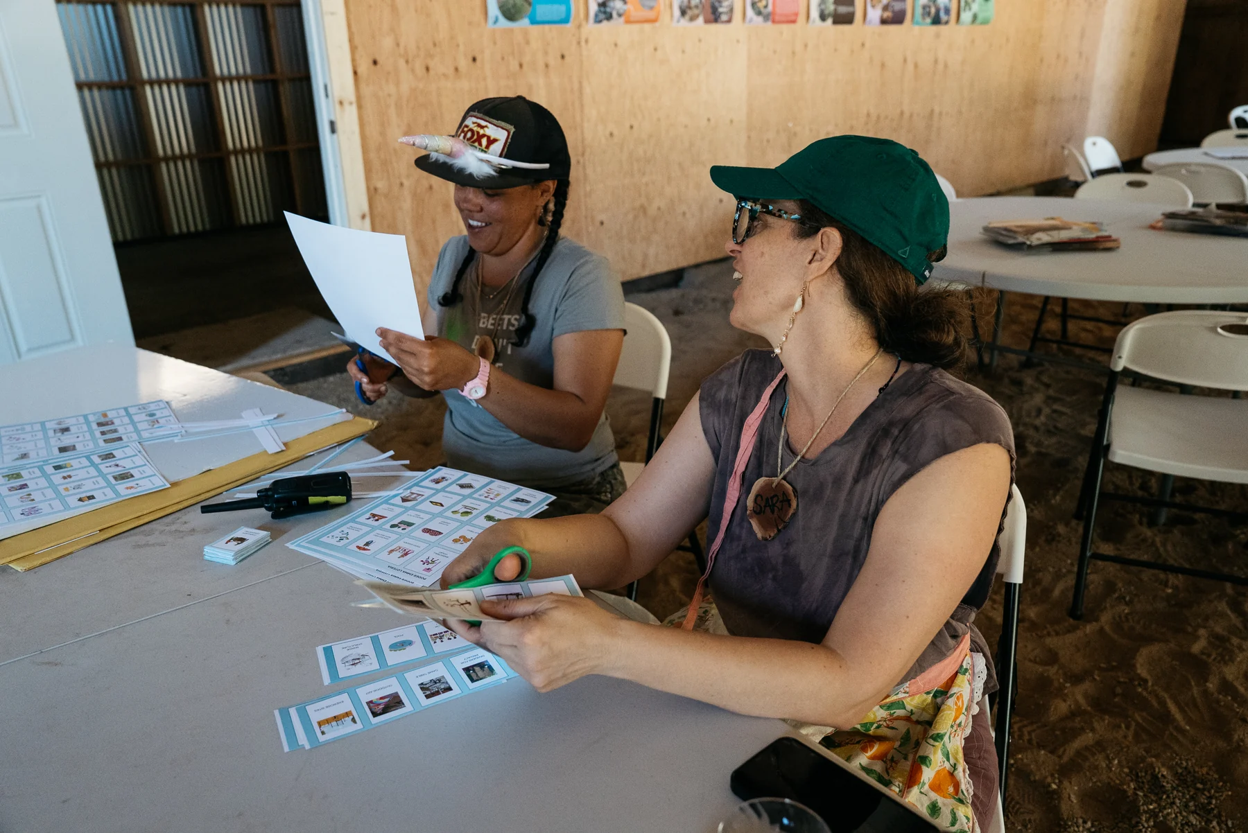 Two participants smile while cutting printed materials at a table.
