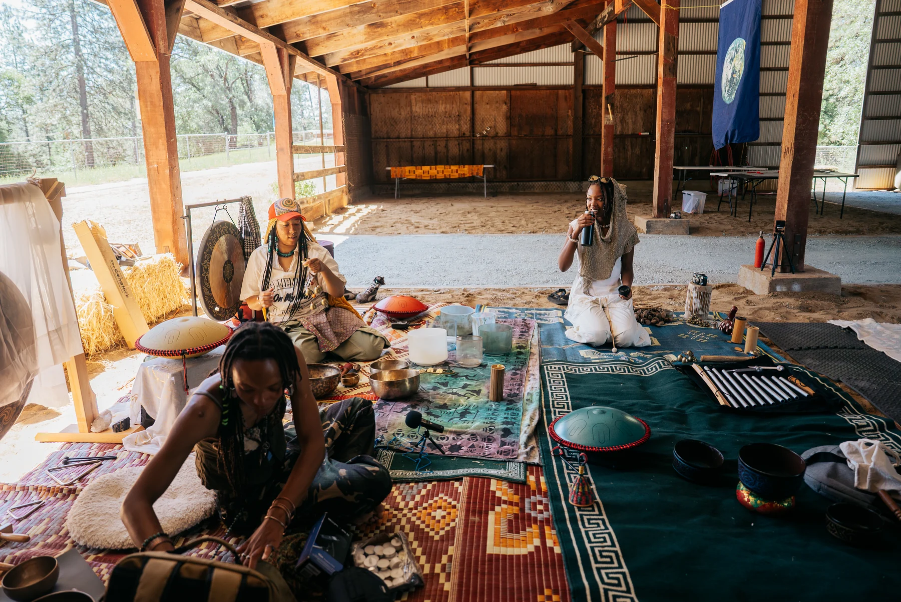 People and percussion instruments arranged on rugs inside an open timber-framed building.