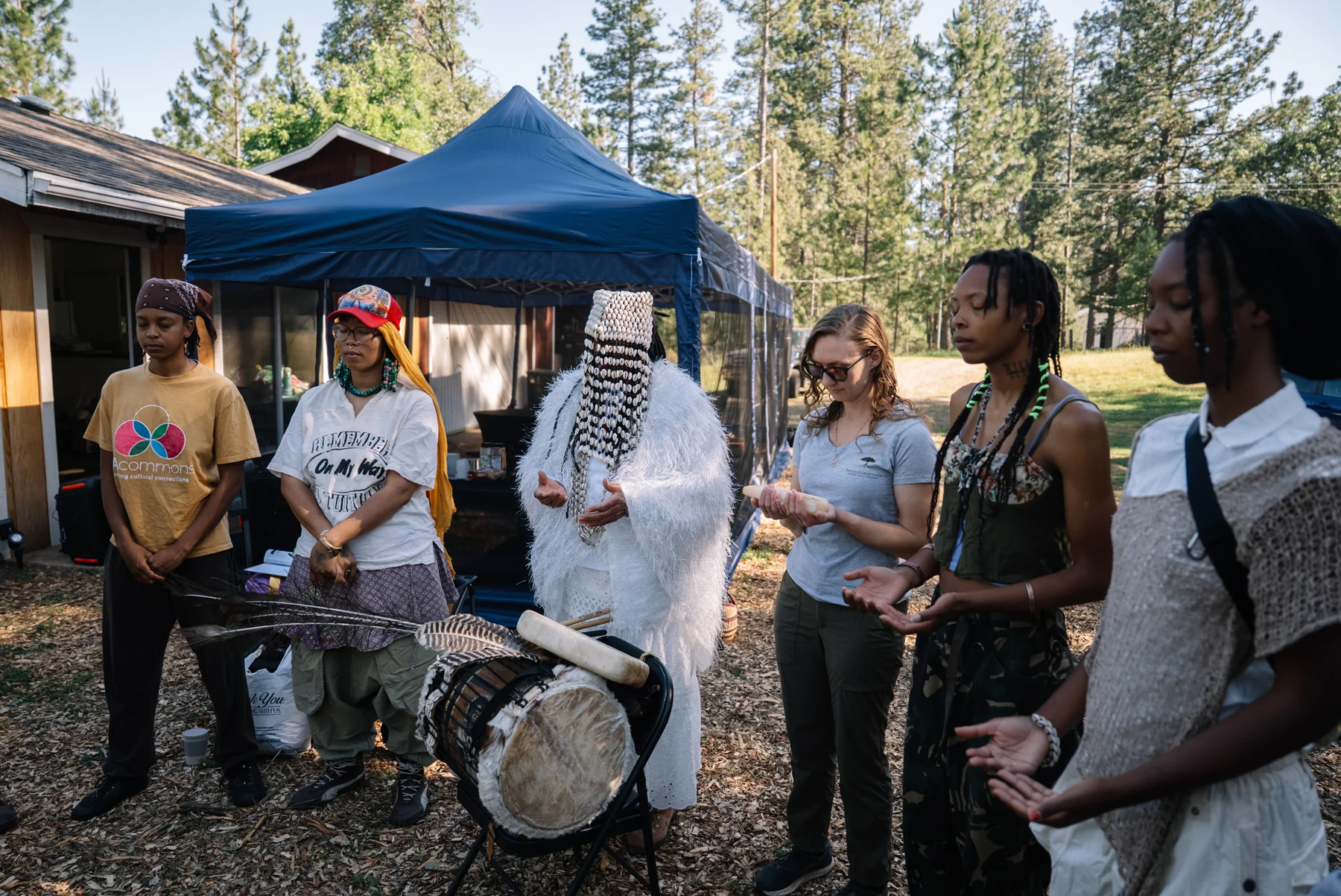 Participants stand in a circle around a drum outdoors.