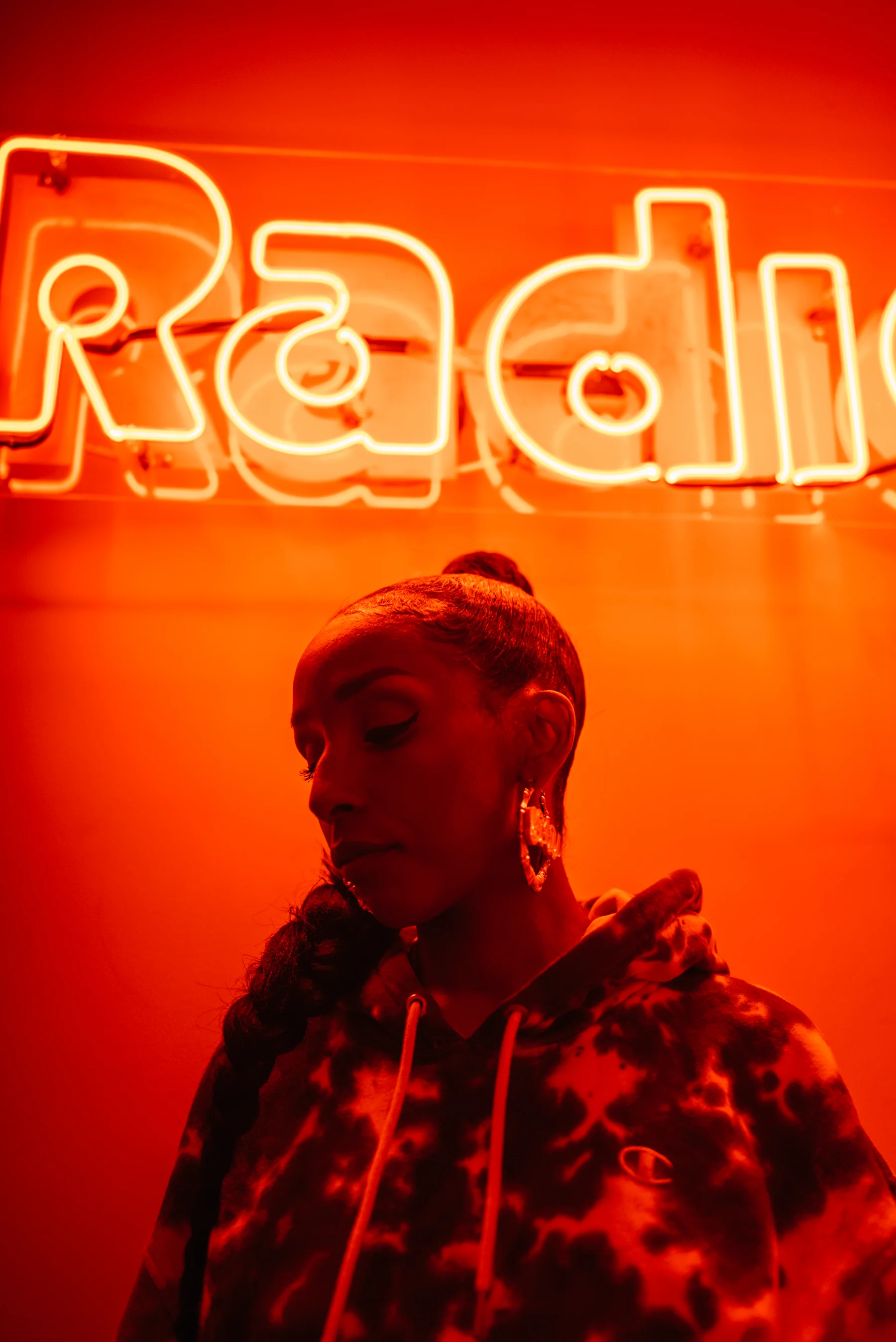 A portrait of ASTU beneath a glowing neon sign, illuminated in vivid red light.
