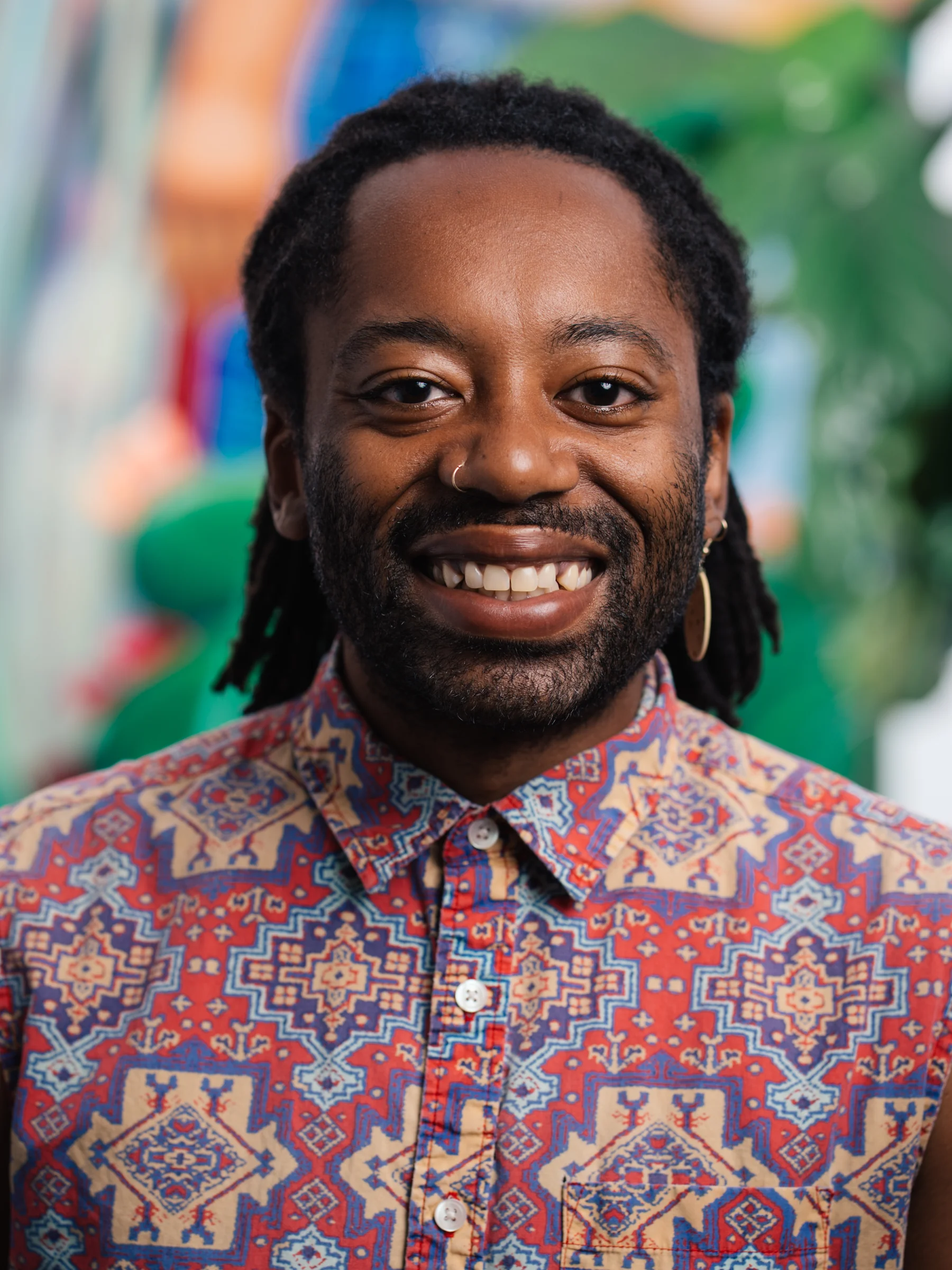 A smiling subject in a red and blue patterned shirt photographed against a colorful mural.