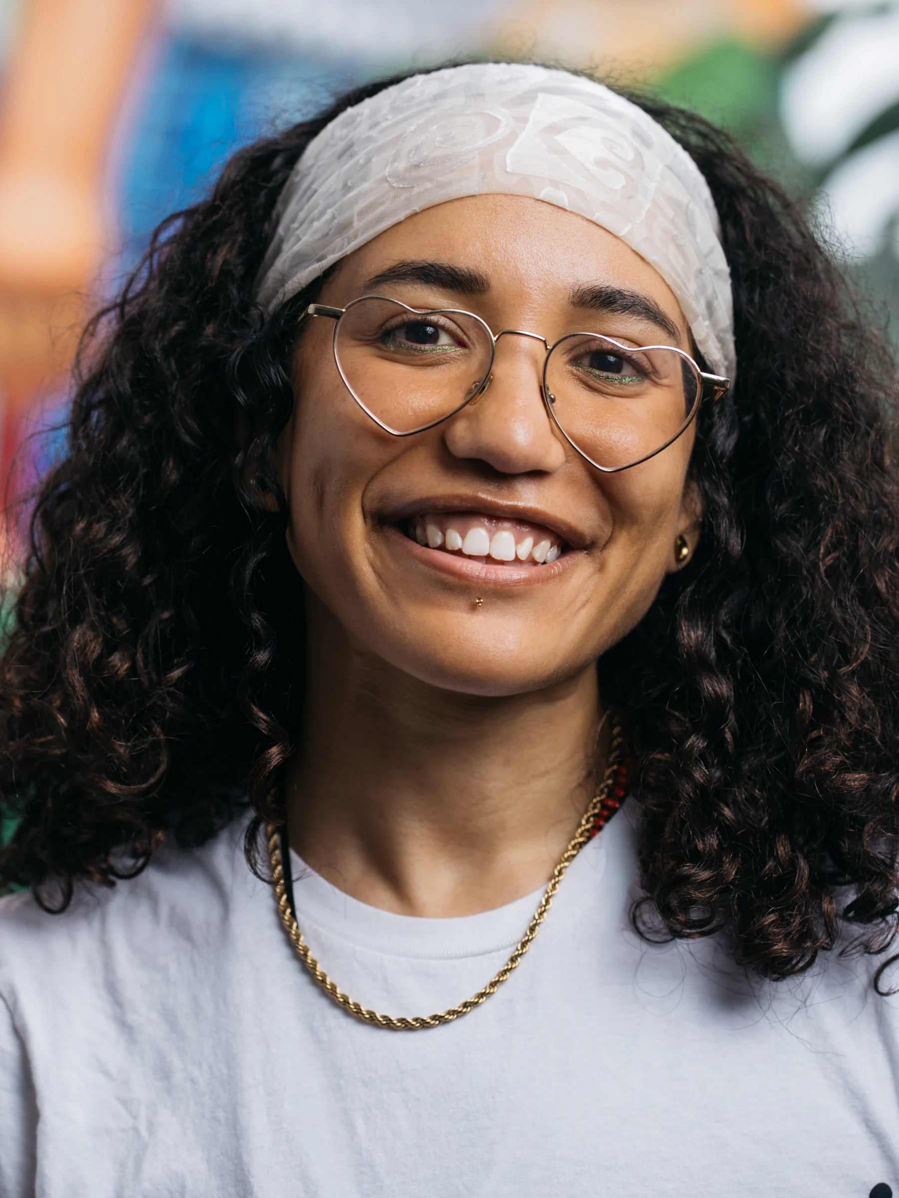 A smiling subject with glasses and a light headband photographed against a colorful mural.