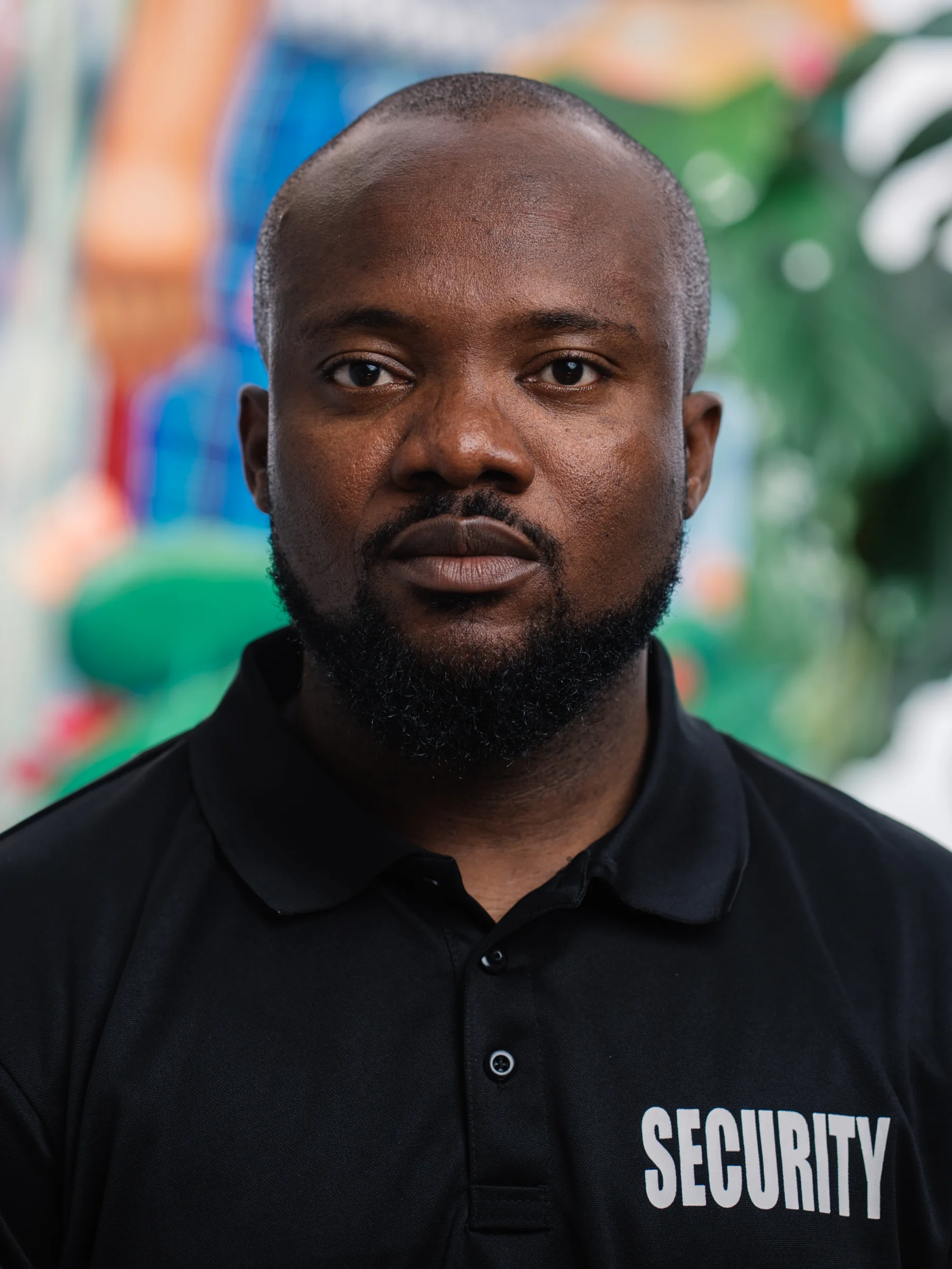 A subject in a black collared shirt looks directly at the camera against a colorful, softly blurred backdrop.