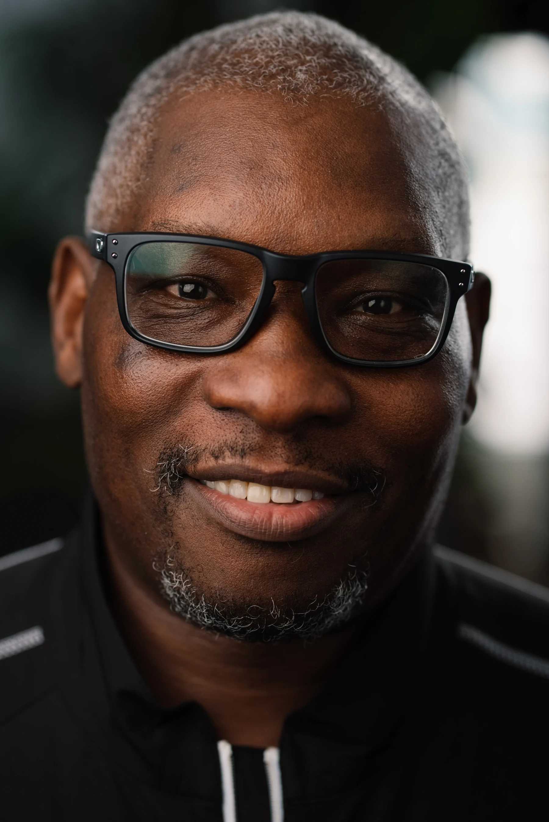 Live Free USA headshot: Smiling subject wearing dark glasses and a black shirt.