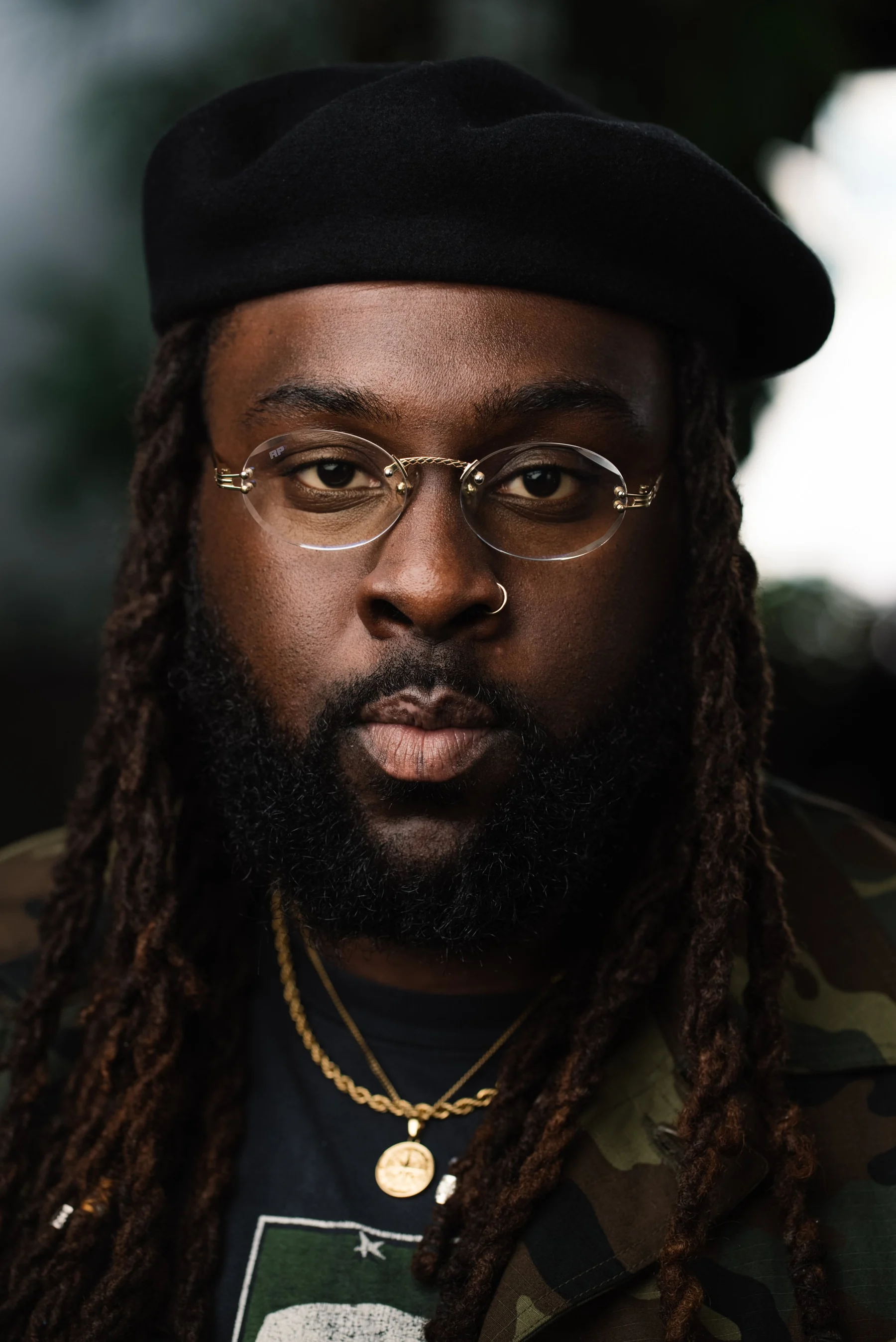 Live Free USA headshot: Subject wearing glasses, a black beret, and gold necklaces.