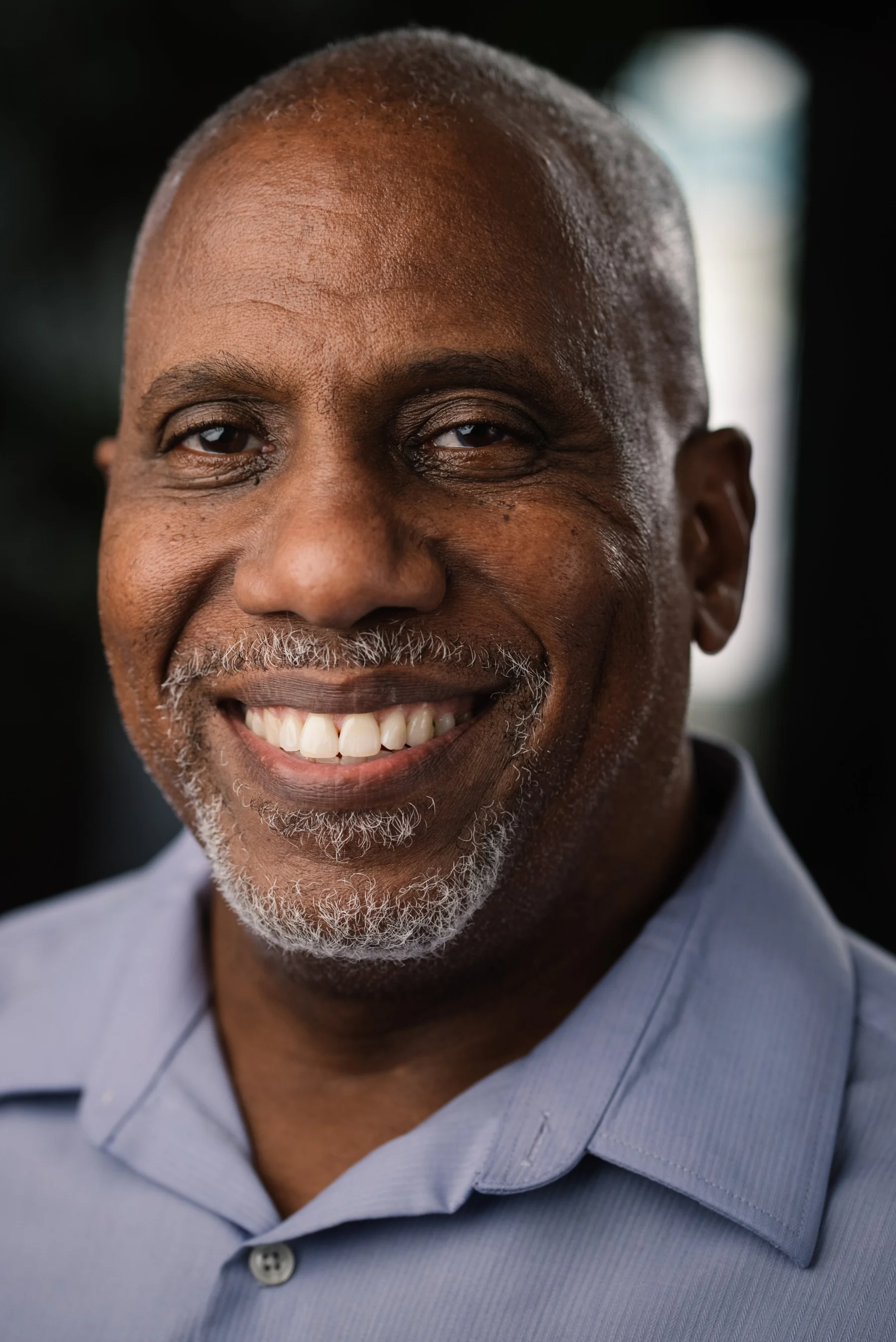 Live Free USA headshot: Smiling subject wearing a pale blue collared shirt.
