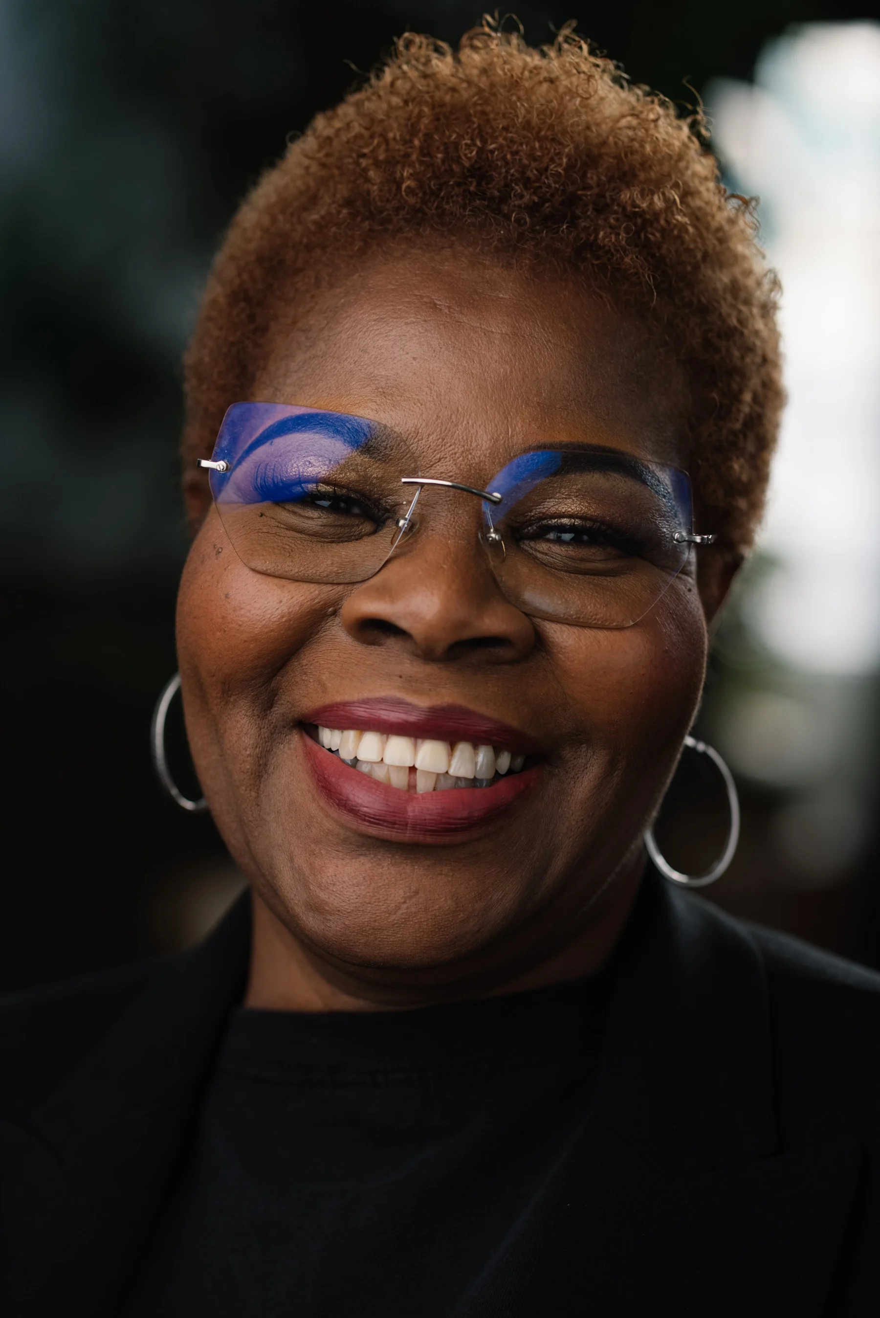 Live Free USA headshot: Smiling subject wearing blue glasses and a black top.
