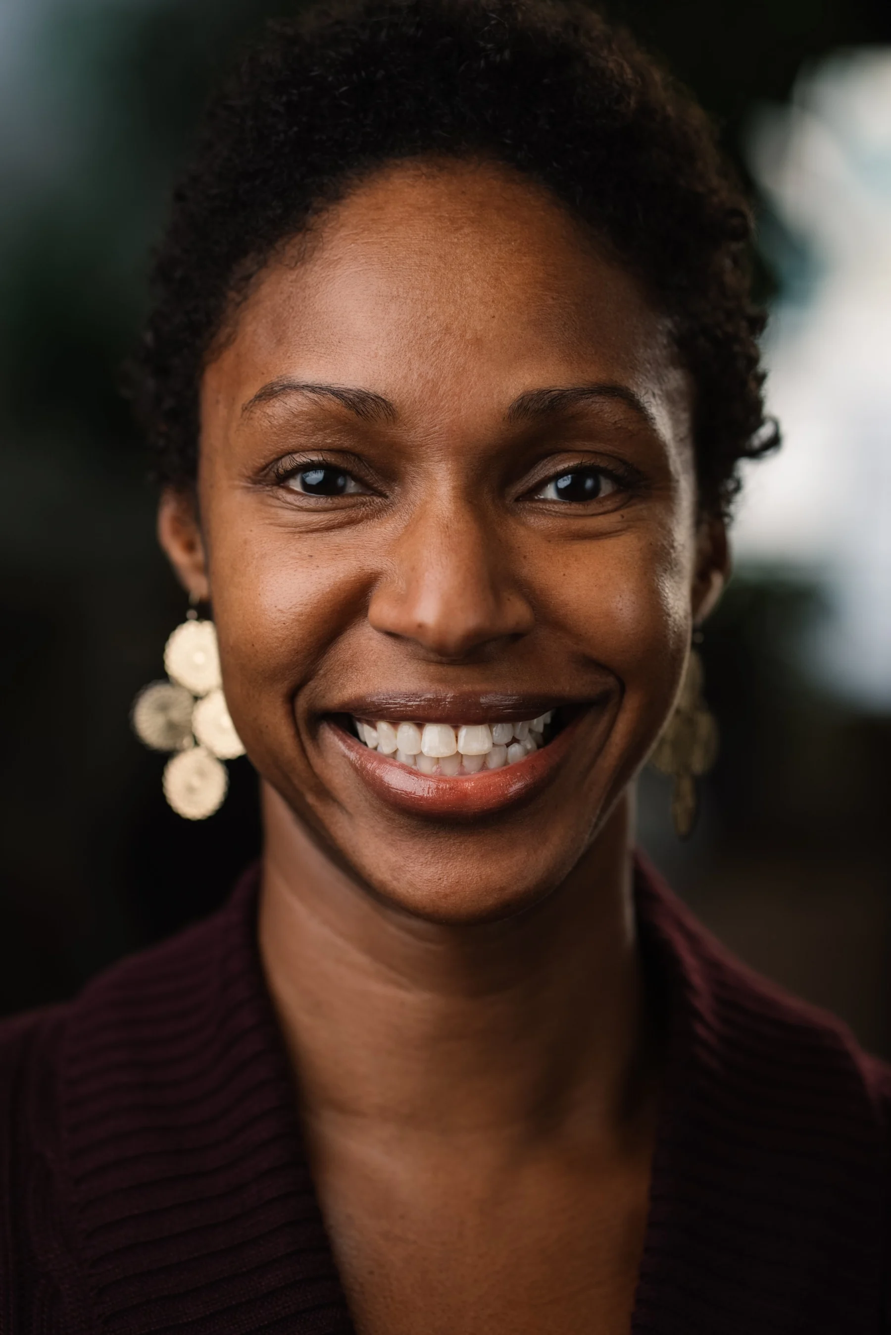 Live Free USA headshot: Smiling subject with short curls and round earrings.