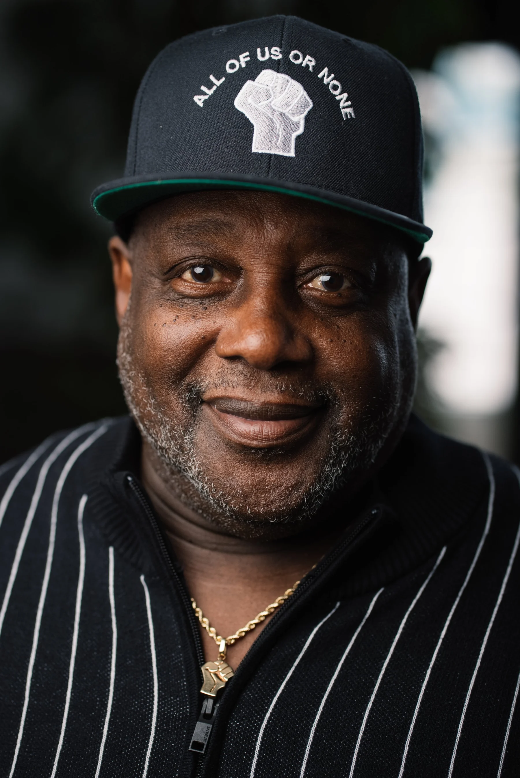 Live Free USA headshot: Smiling subject wearing a black cap and pinstriped shirt.