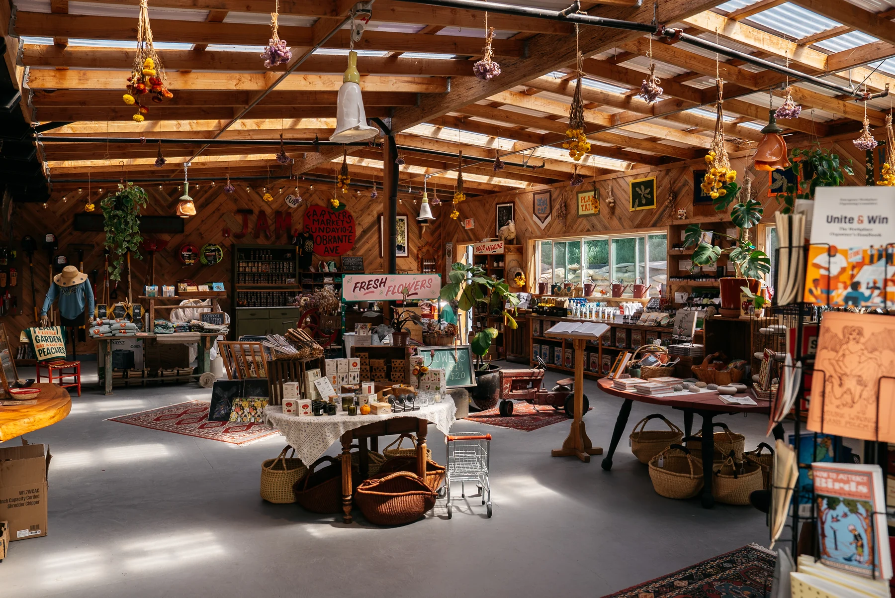 Plants, baskets, cards, and garden supplies fill a wooden farm store beneath hanging dried flowers.