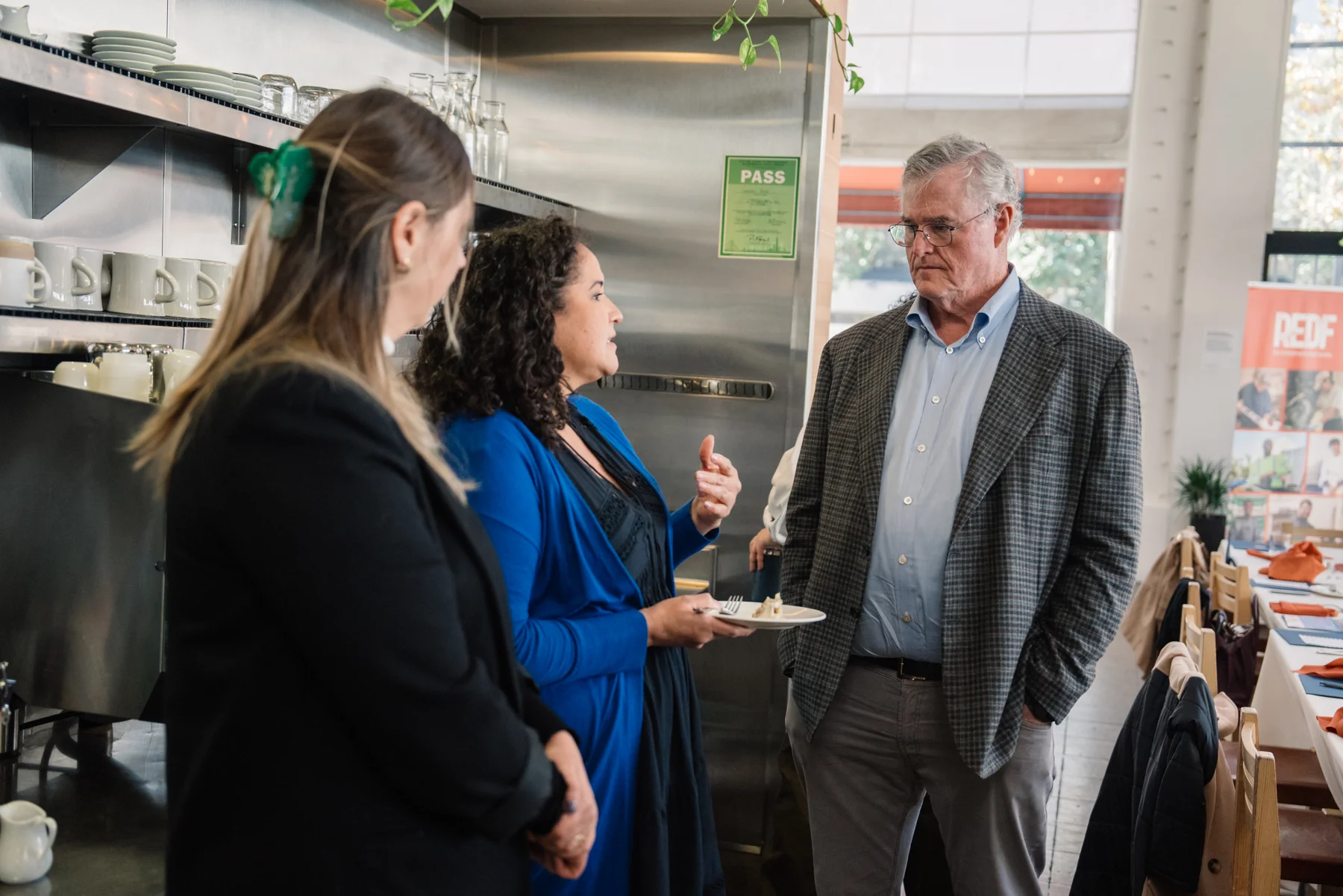 Three attendees talk over small plates beside a kitchen counter.