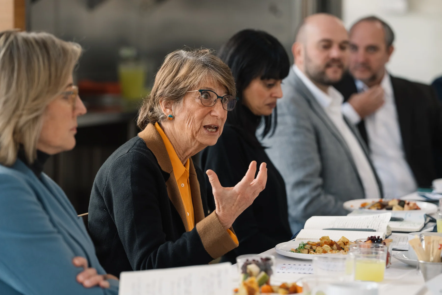 A seated attendee speaks with one hand raised while other participants listen.