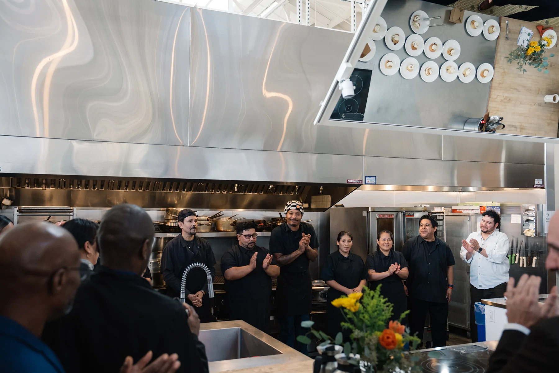 People gathered in a commercial kitchen applaud.