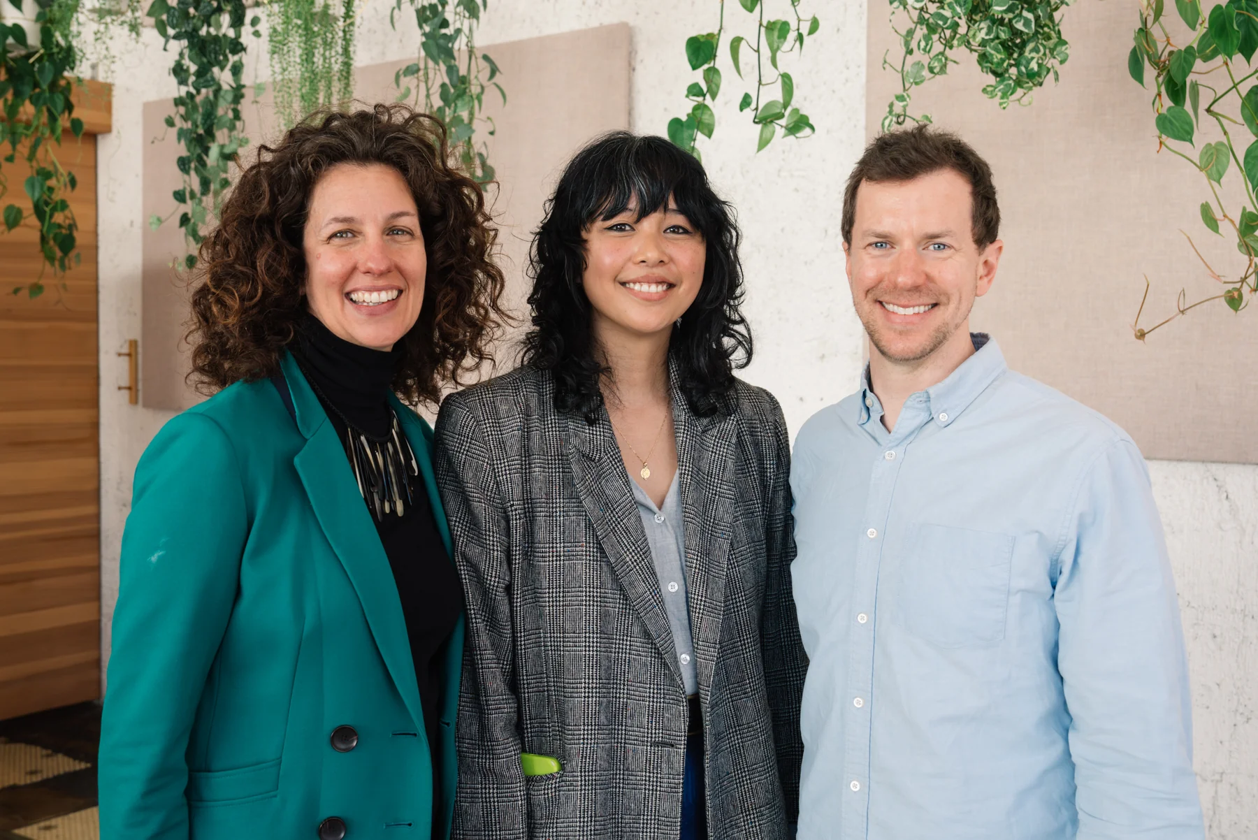 Three smiling attendees pose together in front of trailing plants.