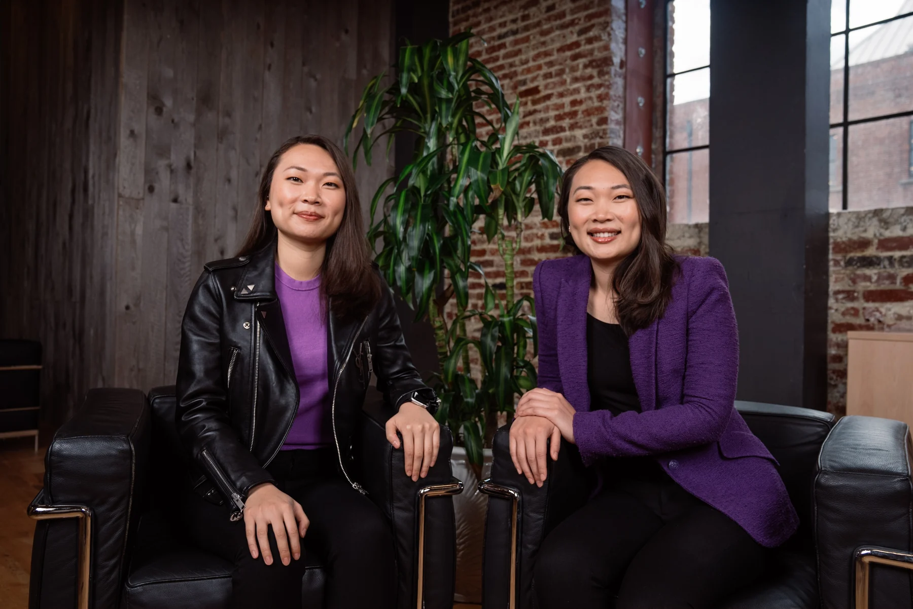 Searchlight's two founders seated together in a brick-walled workspace.