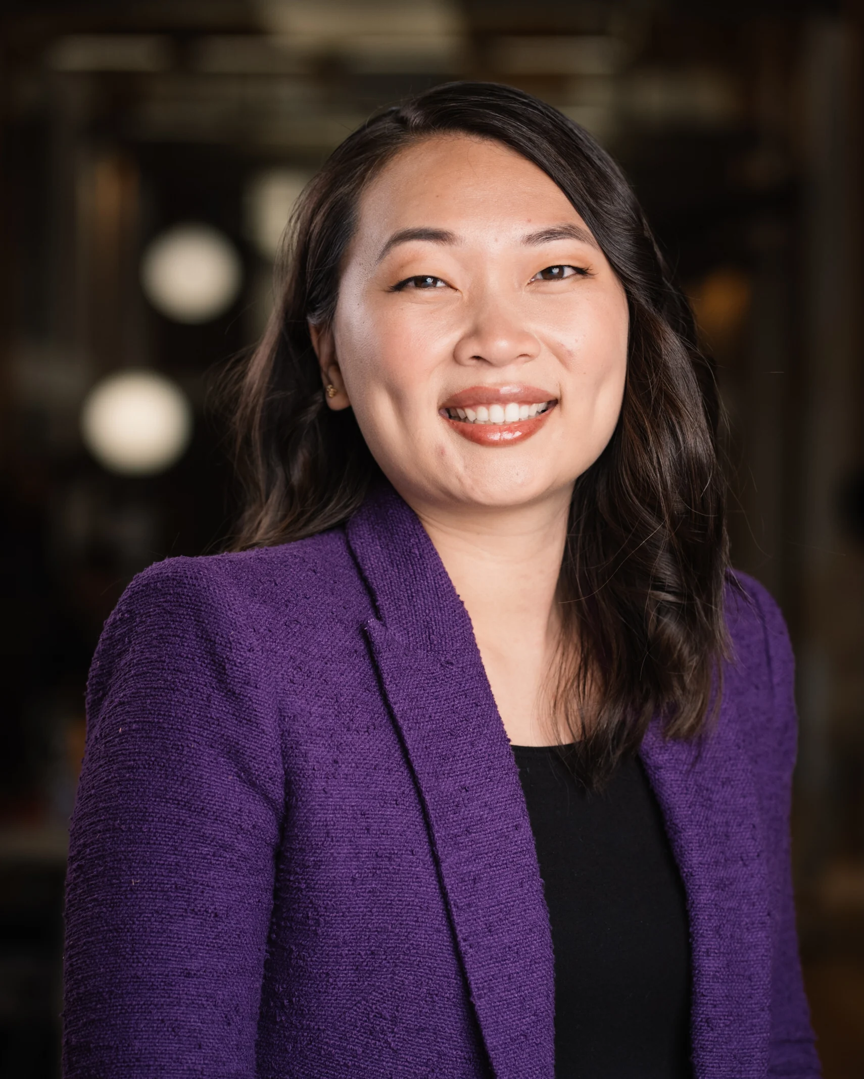 Searchlight portrait with a purple blazer against a softly blurred workspace.