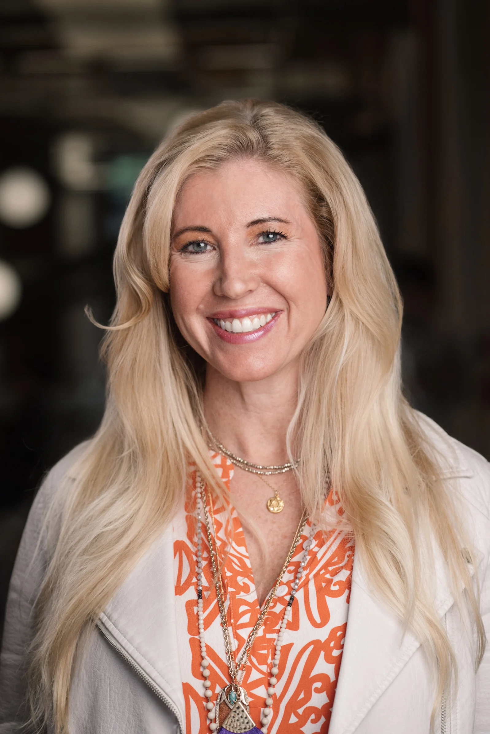 Searchlight portrait with an orange patterned top and a light jacket.
