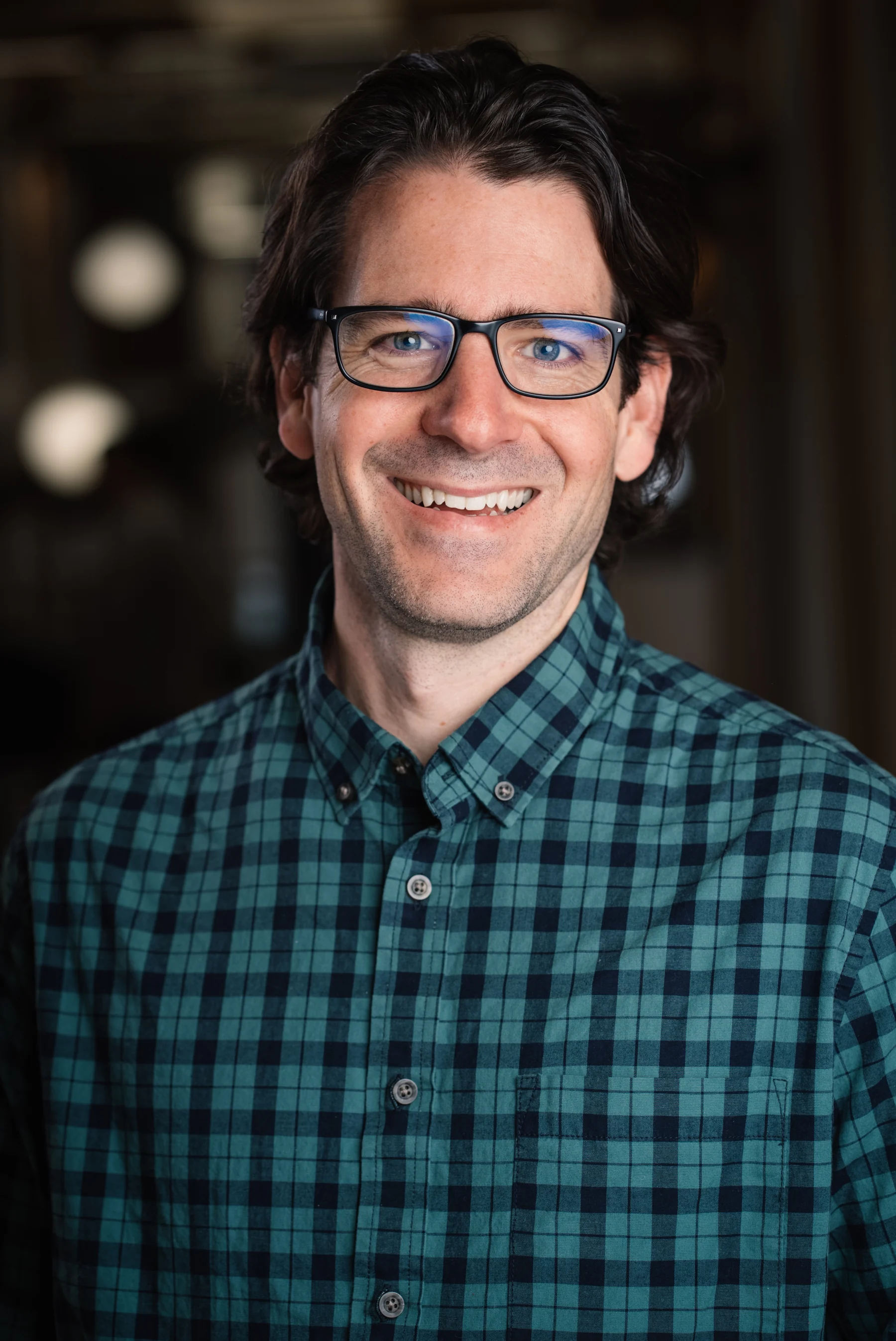 Searchlight headshot with glasses and a green plaid shirt.