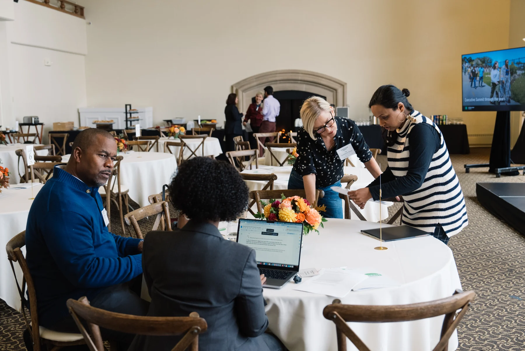 Attendees collaborating around a table with laptops, notes and a bright floral arrangement.